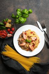 Seafood pasta and dried tomatoes in a creamy sauce with basil and parmesan on a dark background top view.
