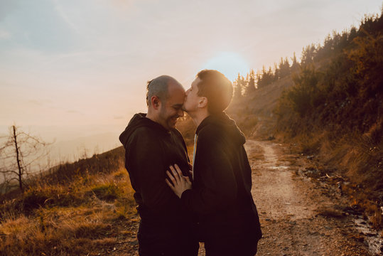 Side view of homosexual couple hugging and kissing on path in forest in sunny day