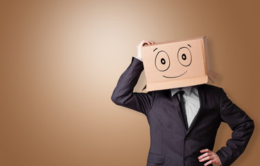 Young man standing and gesturing with a cardboard box on his head with drawn smiley face
