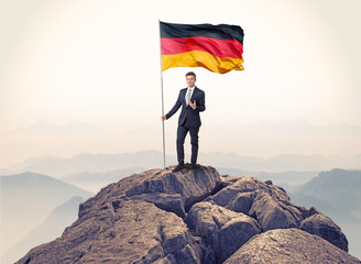 Obraz premium Successful businessman on the top of a mountain holding victory flag 