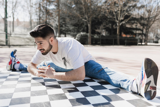 Young bearded guy in casual wear doing leg split in park in sunny weather