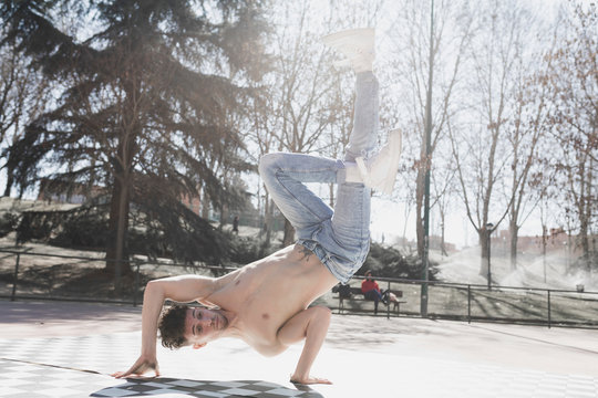 Young athletic guy in jeans practicing break dance in park in sunny weather