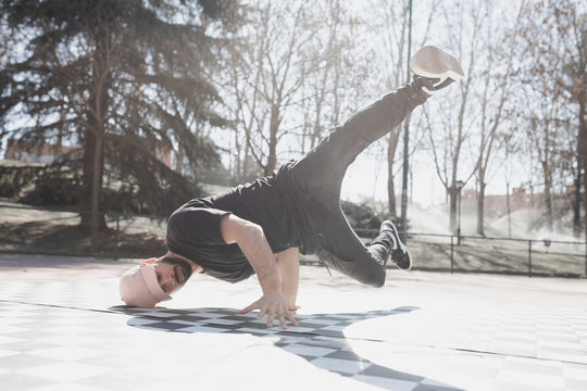 Young athletic guy practicing break dance in park in sunny weather