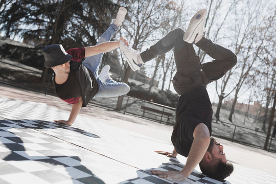Side view of young guys practicing break dance on checkered floor in park in sunny weather