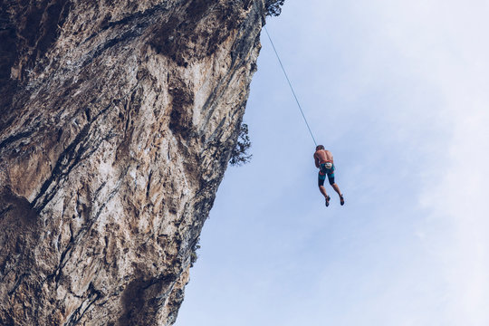 From below unrecognizable climber hanging on rope on rough cliff against blue sky