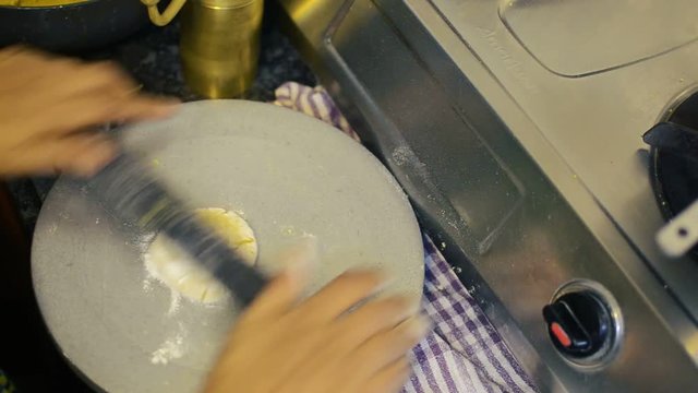 Medium closeup view of a person preparing a Chappathi or Indian bread on a wooden board with rolling pin