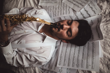 young musician lying playing the saxophone with sheet music around