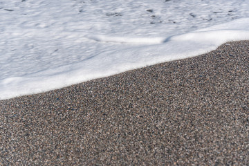 White Foam of Surf on a Black Volcanic Sand Beach in Sicily