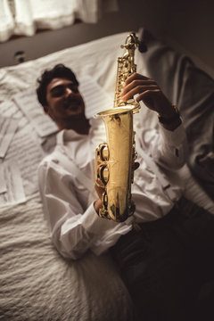 young musician lying playing the saxophone with sheet music around