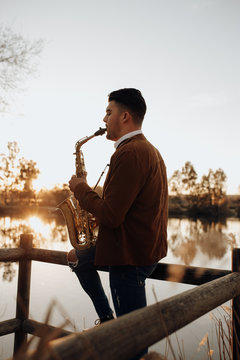 young musician playing the saxophone at sunset in the lake