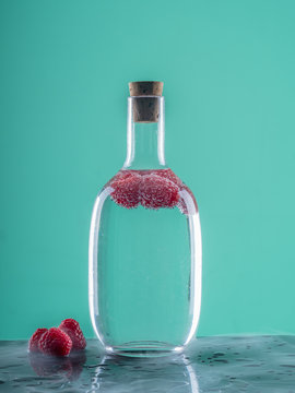 Glass bottle with blue beverage near berries on board on abstract background
