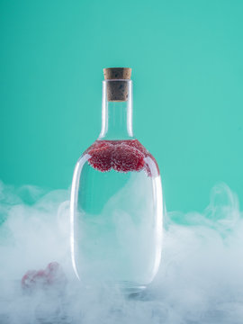 Glass bottle with berries and alcohol on board between mist on azure background