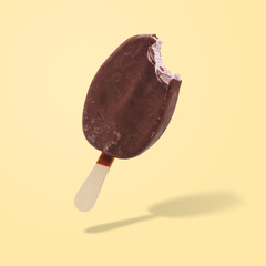 Bitten ice cream popsicle on a stick in chocolate on a yellow background