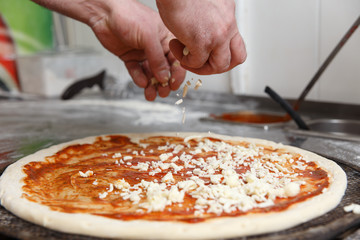 The hands of chef sprinkles the pizza with cheese
