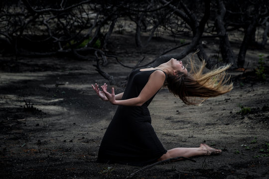Side view of young ballerina in black wear posing on land between dry woods