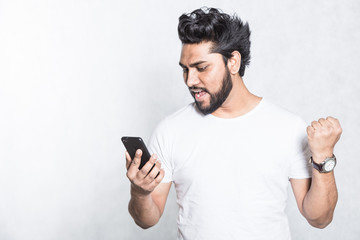Happy young man holding smartphone and celebrating his success.