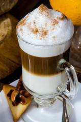 glass latte with foam. standing on a wooden table, against the background of oranges and orange juice