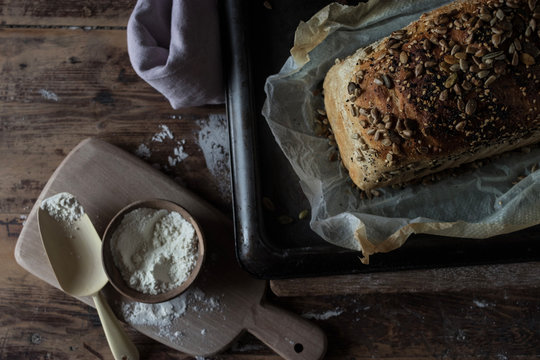 Loaf of delicious rye bread with seeds lying on timber tabletop near raw flour