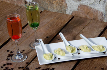 On a wooden table in a champagne glass red and green cocktail. and there is a plate with a snack