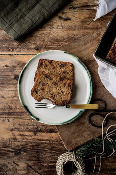 From above slices of healthy banana bread near fork on dish on cutting board near scissors, napkin and threads on wooden background