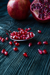 Healthy fresh pomegranates on a dark wooden background. A spoon with grains of fresh pomegranate. Vibrant focus. Dark wooden background. Side view.