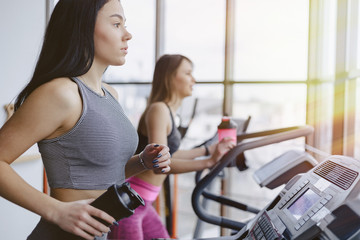 Girls in the gym are trained on treadmills and drink water, smiling