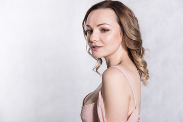 Fototapeta premium Portrait of beautiful young elegant female in pale pink wedding dress with big neckline, on a white background.