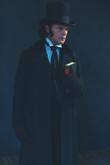 Edwardian man in long black coat and hat holding book.