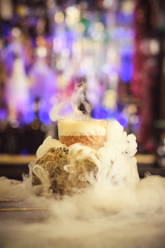 Cup of delicious cocktail emitting thick steam while being placed on counter on blurred background of bar