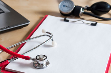 Red stethoscope on a red clipboard. Near laptop and tonometer. Right copy space. Medical device. Treatment, health care. Heart examination. Studying the pulse. Close-up.