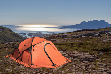 Camping im Fjell, in den Bergen, oranges Zelt mit Blick über die Felsen auf den Ozean, verlassene Gegend