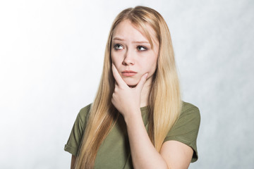 Embarrassed unsure young woman holds her chin and purses his lips, looks incredulously, tries to make a decision.