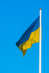 Photo of a flag of Ukraine are sways in the wind on flagpole against a background of clear blue sky