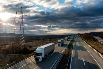 Caravan or convoy of lorry trucks on country highway under a beautiful sky