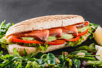 Sandwich with red fish, eggs, avocado, fresh vegetables and greens on black shale board over black stone background. Healthy food concept
