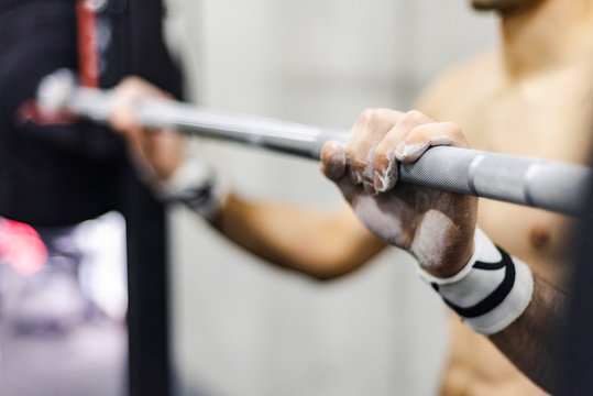 Crop shirtless male lifting barbel wit h weights in gym on blurred background