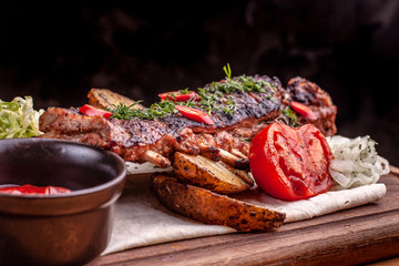 Delicious barbecued ribs seasoned with fresh herbs, cabbage salad, backed potato on an old rustic wooden chopping board