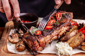 Delicious barbecued ribs seasoned with fresh herbs, cabbage salad, backed potato on an old rustic wooden chopping board