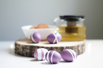 lilac Easter eggs on wooden stand with tea and cookies