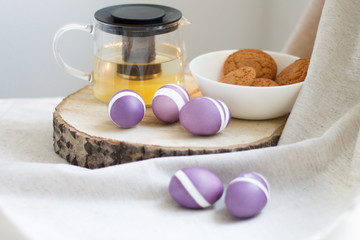 lilac Easter eggs on wooden stand with tea and cookies
