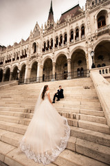 Obraz premium Bride and groom hugging in the old town street. Wedding couple walks in Budapest near Parliament House. Bride and groom on the stairs