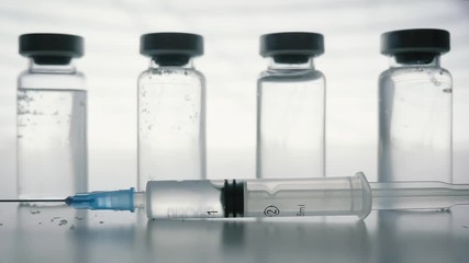 Plastic Syringe falling in slow motion in front of glass vaccine bottles. Mandatory vaccinations are currently a hotly debated topic with the anti-vaxx movement believing vaccines cause autism.