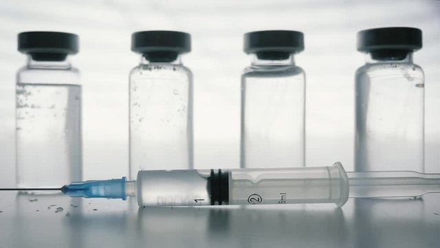 Plastic Syringe falling in slow motion in front of glass vaccine bottles. Mandatory vaccinations are currently a hotly debated topic with the anti-vaxx movement believing vaccines cause autism.