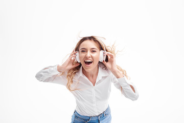 Young woman listening loud funny music hits on the radio in headphones. Glad girl in casual clothes posing with hair waving and laughing. having fun on white studio background