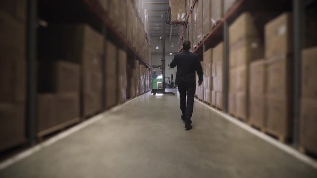 Medium shot of businessman walking and talking on smart phone in warehouse
