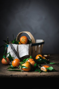 Ripe orange mandarins and basket with towel on rough wooden table