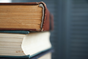 Extreme close-up of a stack of old books, yellowed pages, a broken back of a book against a gray bookcase, soft focus.