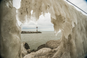 Looking through ice that has formed on edge of rock and in the distance, you'll notice a jetty. Geneva State Park located on the shores of Lake Erie in Ashtabula County, Ohio.