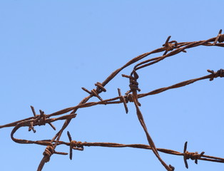 Rusty barbed wire and blue sky background.