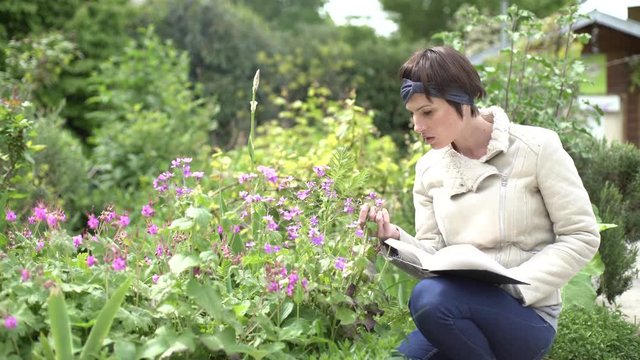Medium shot of woman examining flowers through a book in the garden